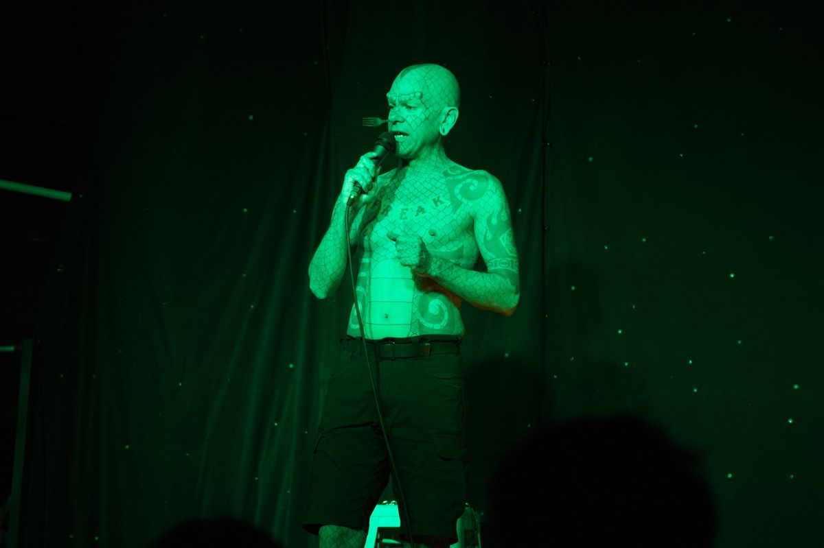 Tattooed man with fork up his nose.