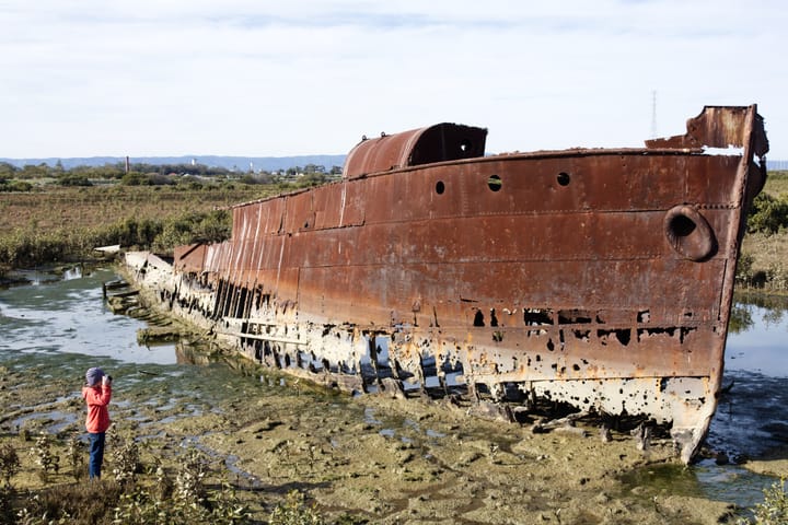 Boy photographing a rusty shell of a ship